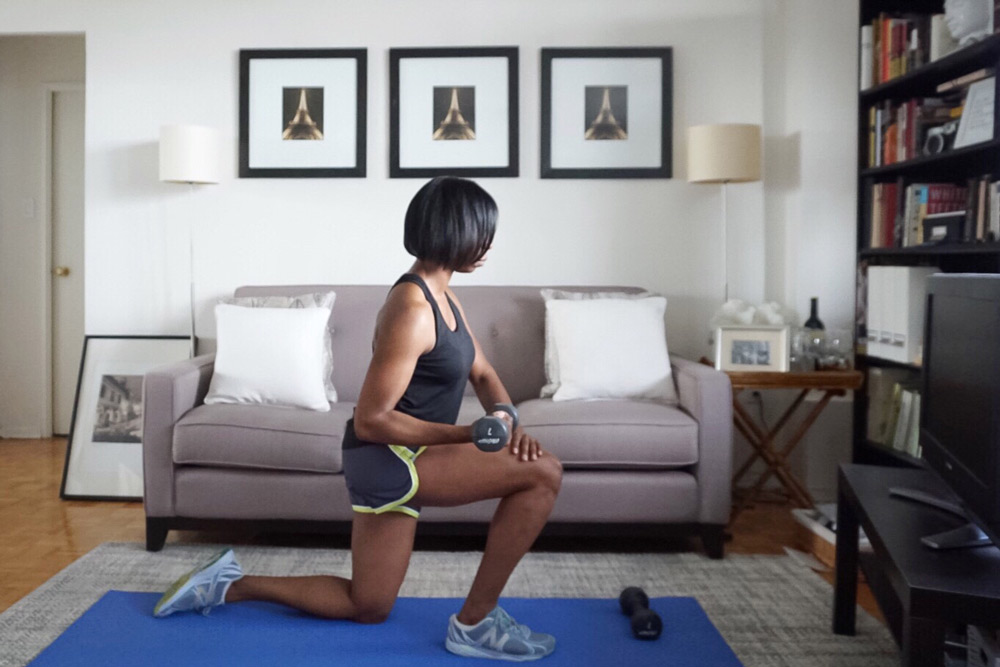 woman kneeling on yoga mat performing single arm bicep curl in living room